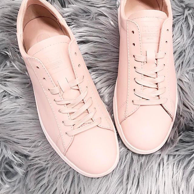 A pair of pink leather sneakers with laces placed on a fluffy, gray textured surface.