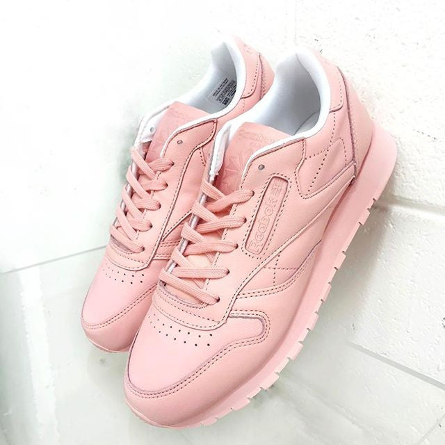 A pair of light pink sneakers with matching laces, a white interior, and cushioned soles. The shoes have subtle stitching details and are displayed against a white background.