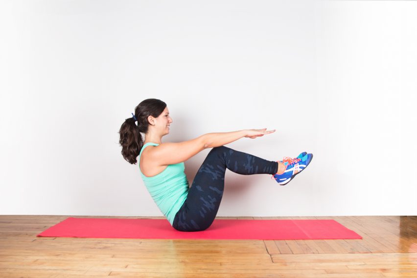 Person exercising in a seated yoga pose on a red mat. They're balancing on their tailbone with legs bent, arms extended forward, wearing a teal tank top, dark leggings, and colorful sneakers.