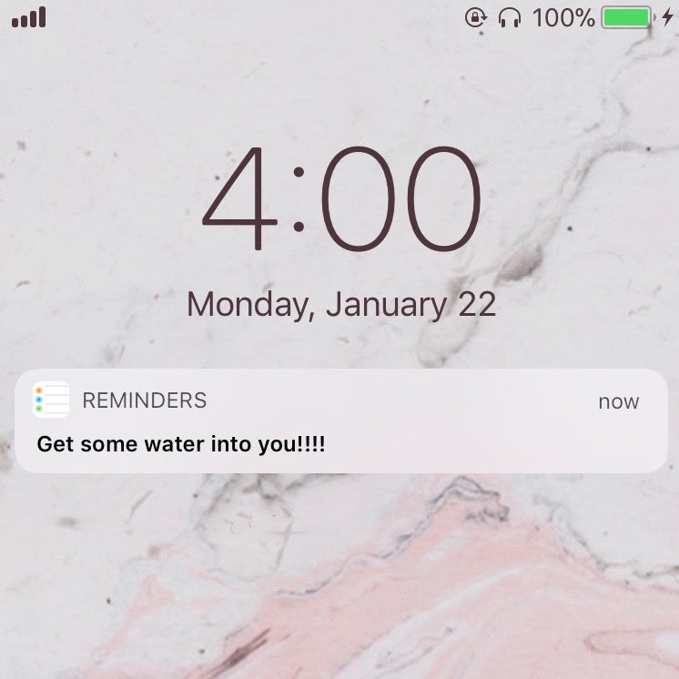 Phone lock screen showing time as 4:00, date as Monday, January 22. A notification from the Reminders app reads, "Get some water into you!!!!" The background is a marble pattern with pink and white tones. Battery icon shows 100% charged.