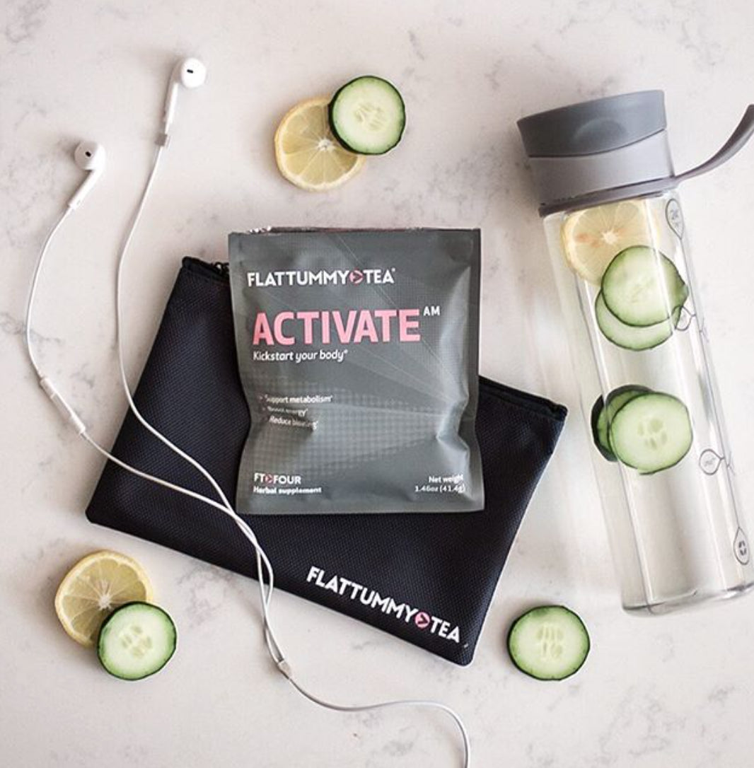 Flat Tummy Tea Activate Tea package on a marble surface with cucumber slices. A clear water bottle filled with cucumber water, white earphones, and a black pouch are nearby.
