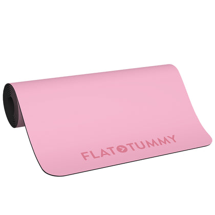 A rolled-out pink Fitness Mat from Flat Tummy Co, featuring the bold, uppercase words "FLAT TUMMY" on one side. The mat is designed with black edges and a non-slip surface, ideal for both home and gym use. The background is plain white, free of any additional objects or decorations.