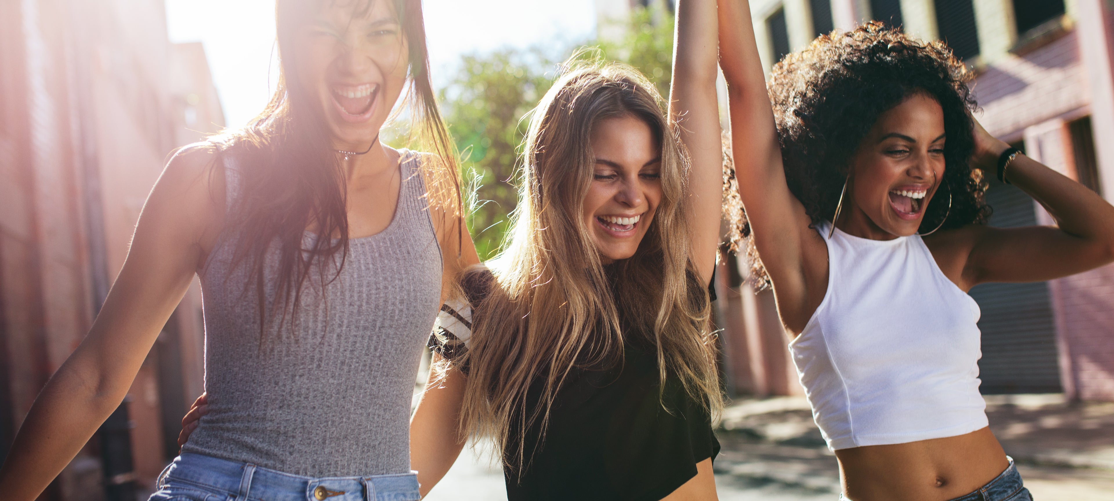 Three joyful women walking arm-in-arm, embodying the positive and empowering mission of Flat Tummy Co.