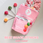 The image shows a pink Flat Tummy Lollipops bag, branded by Flat Tummy Co, surrounded by several colorful lollipops. The bag is partially open, revealing more lollipops inside. Infused with Satiereal to help control hunger, these treats make it easy to beat snack attacks.