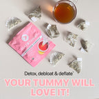 A flatlay image of Flat Tummy Co's Flat Tummy Cleanse package in vibrant pink, surrounded by several tea bags and a cup of brewed tea. Text reads "Detox, debloat & deflate" and "YOUR TUMMY WILL LOVE IT!". This colon cleanse formula will leave your stomach feeling refreshed and renewed.